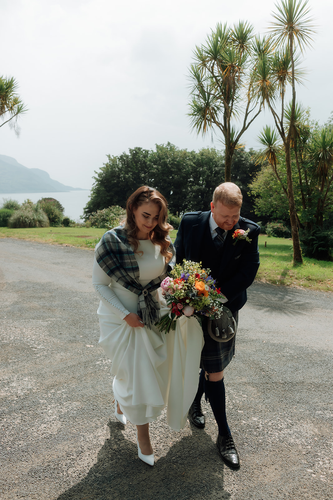 Bride in white dress with colourful bouquet walking with groom on the Isle of Arran