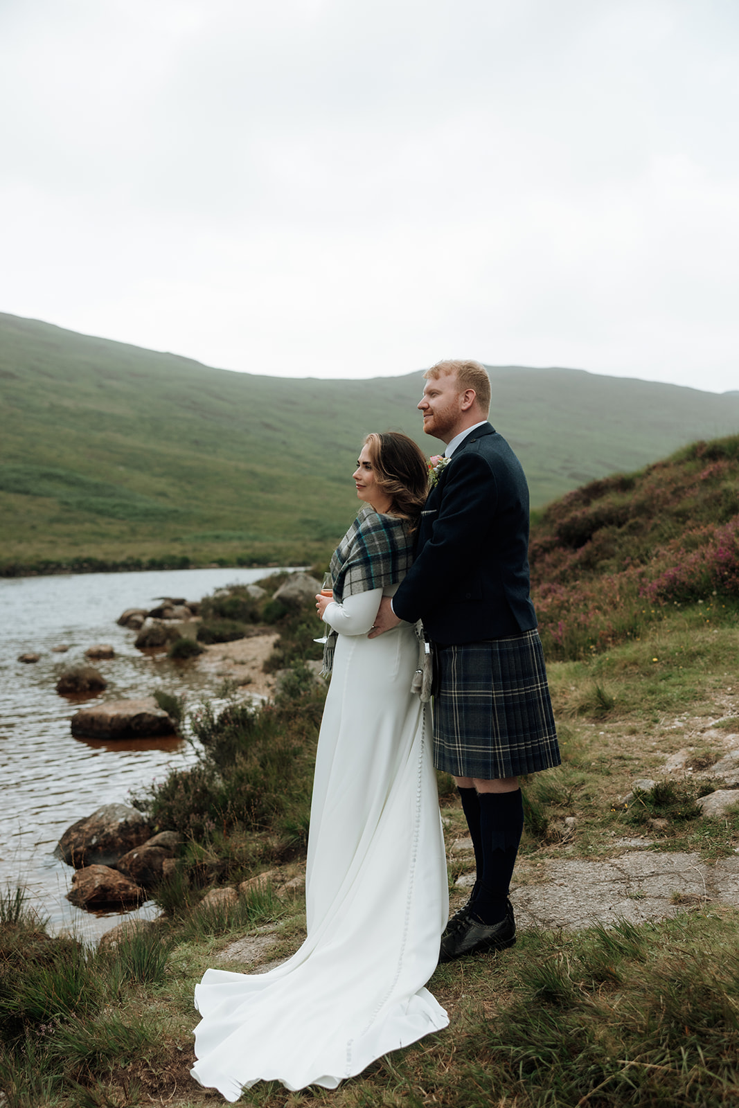 Bride and groom standing by stream with hills behind on Isle of Arran.