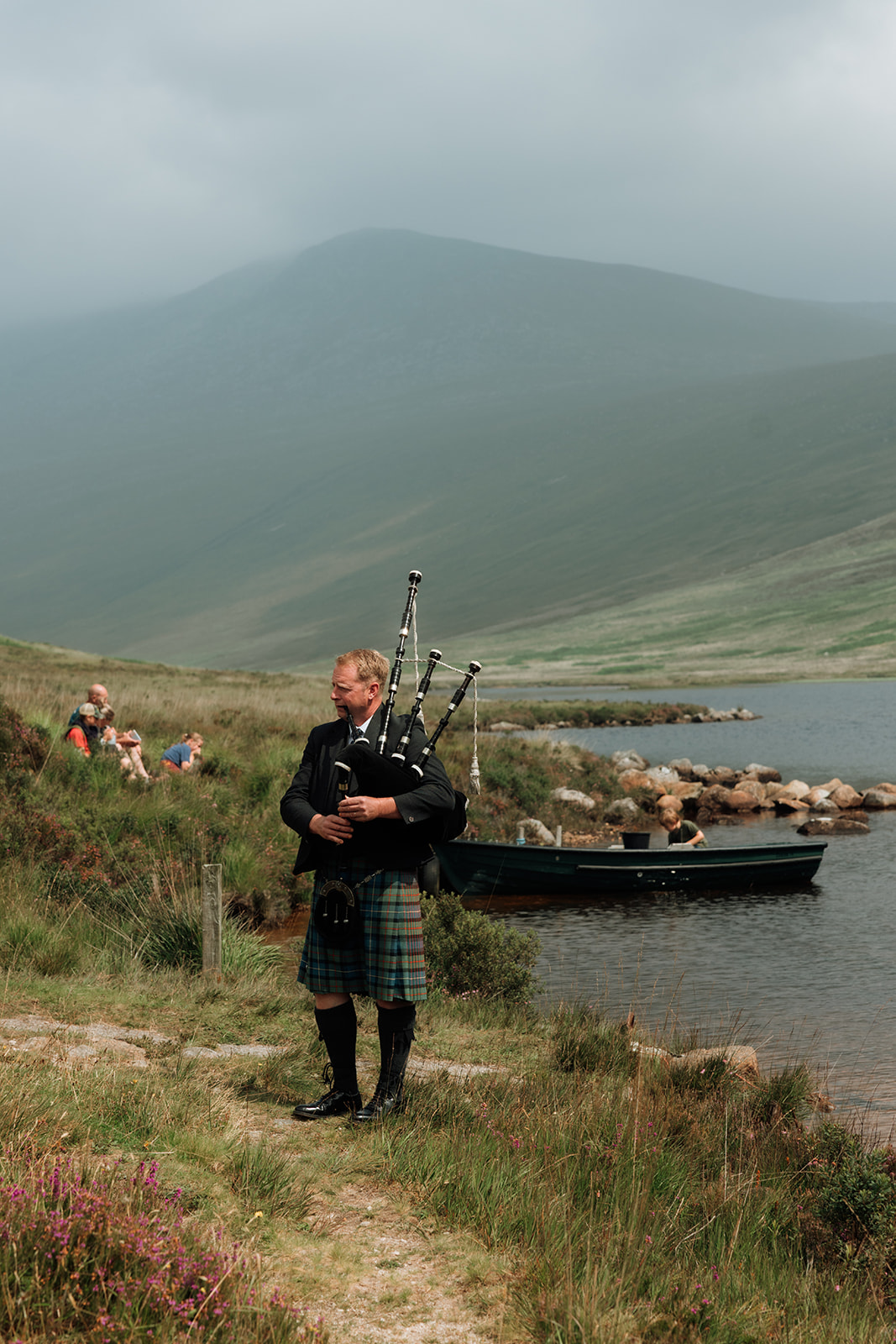 Piper in kilt standing on hillside by Loch Iorsa, Isle of Arran.