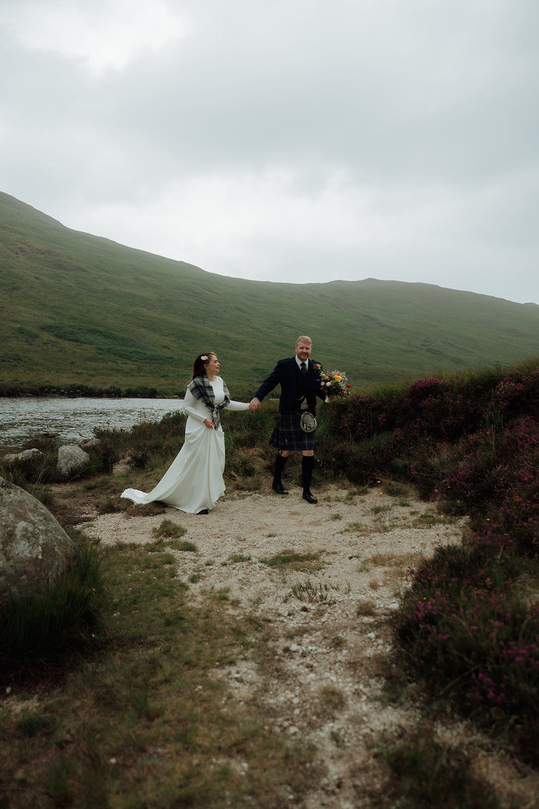 Bride and groom walking by hillside at Loch Iorsa, Isle of Arran.