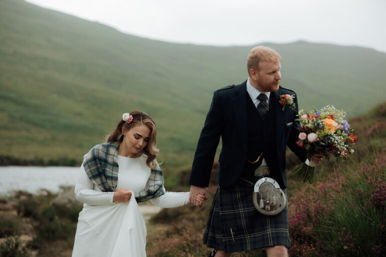 Bride carrying bouquet walking with groom during Isle of Arran elopement.