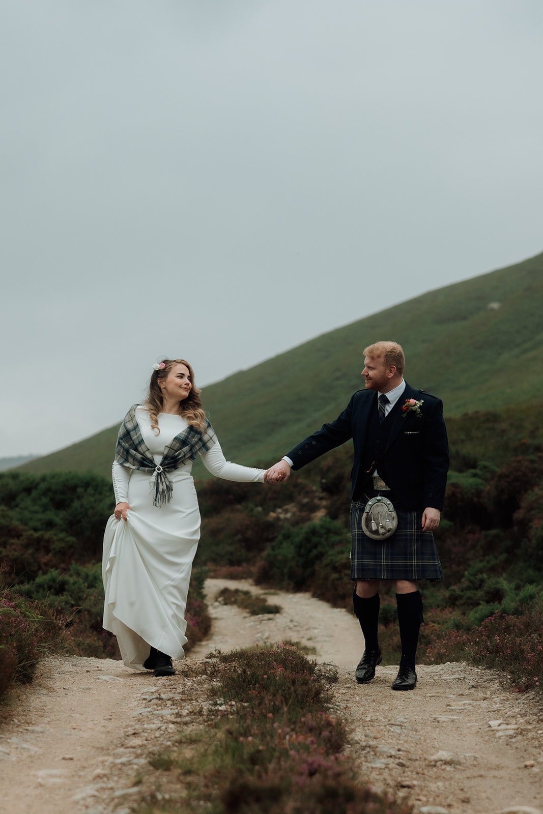 Bride and groom holding hands walking uphill during Isle of Arran elopement.