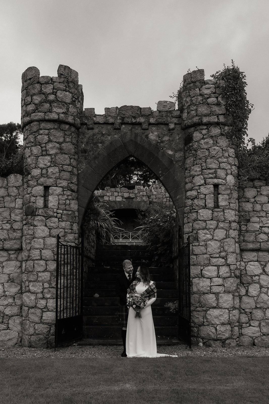 Black and white photograph of bride standing at stone arch during Isle of Arran elopement.