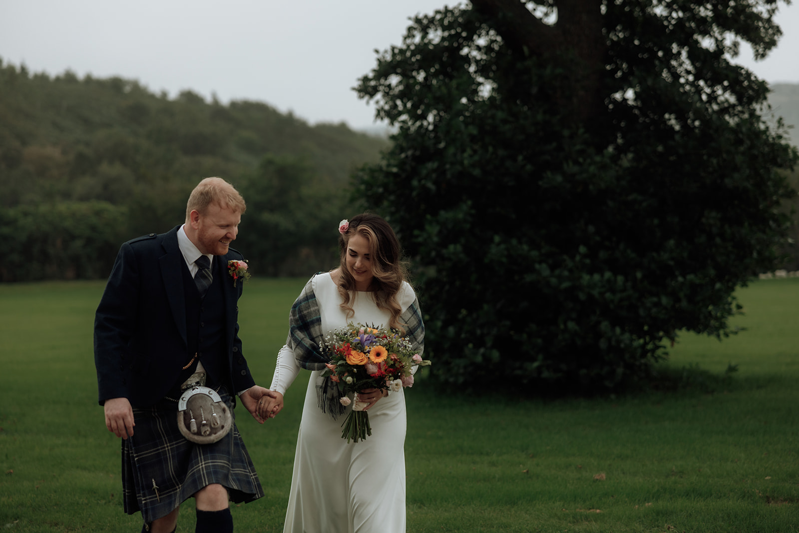 Bride and groom walking across grass smiling during Isle of Arran elopement.