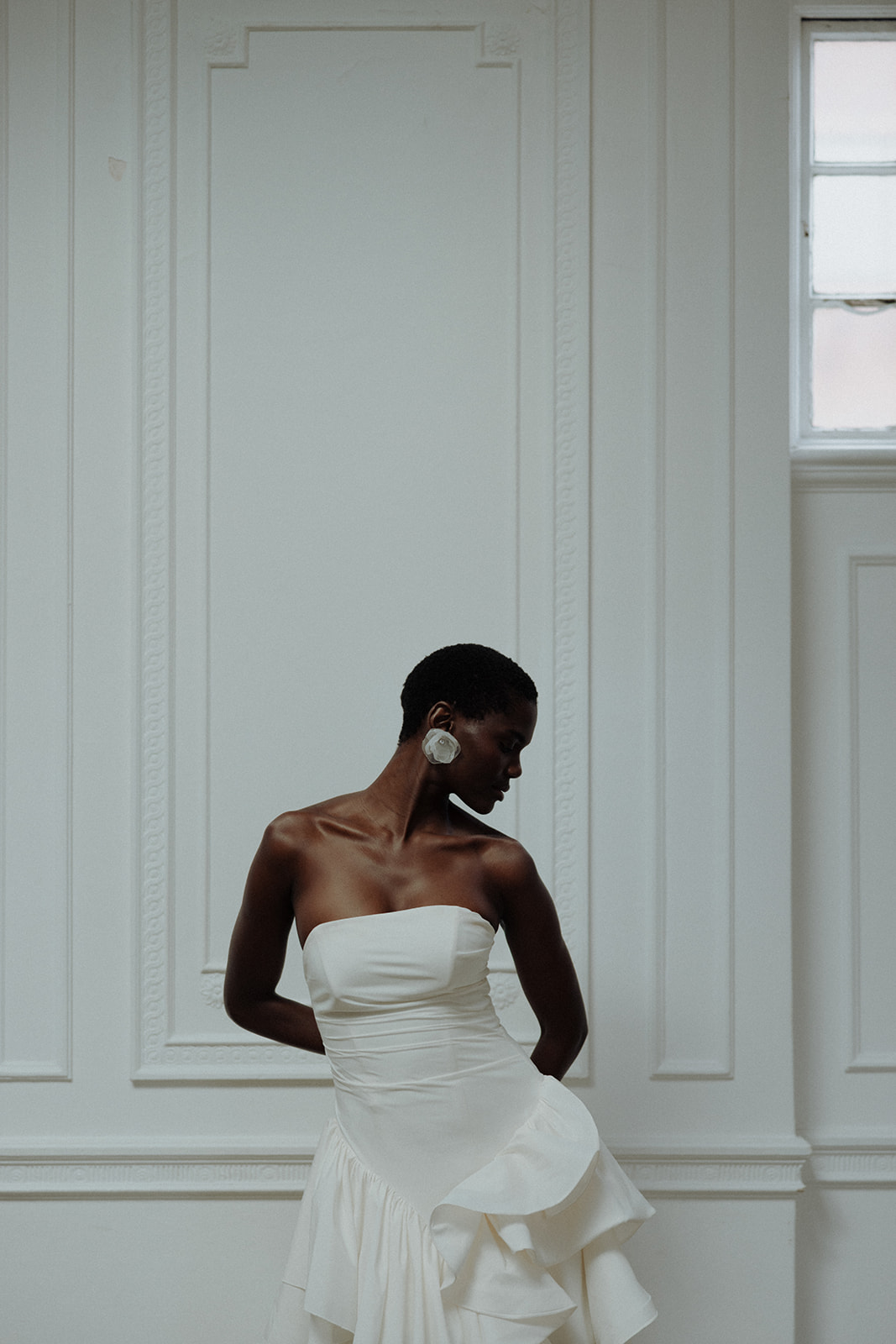 Bride in strapless Darla Haute Couture gown posing against white wall, modern editorial portrait.
