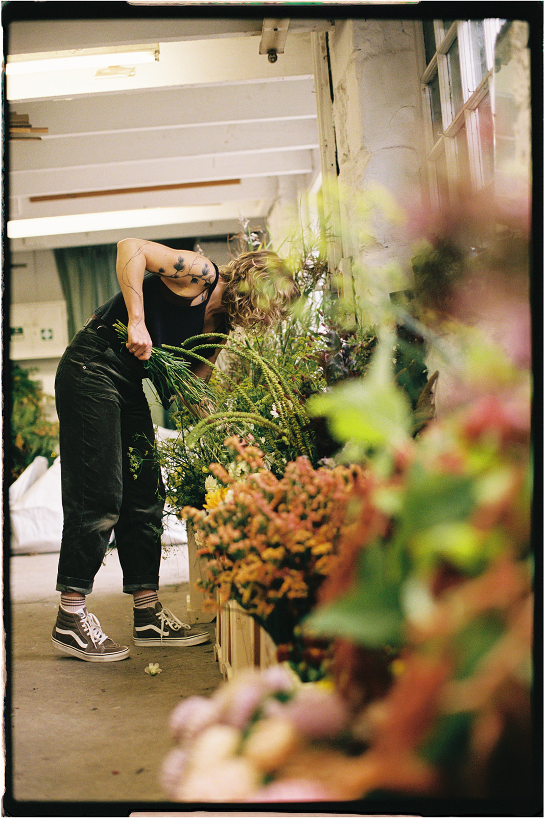 Florist arranging tall floral branches in the studio, captured in soft focus on 35mm film.