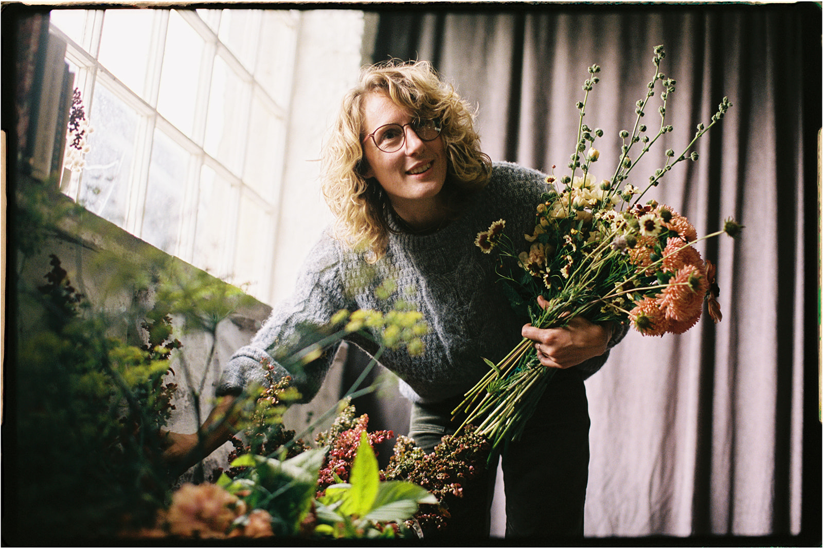 Tupelo Tree florist smiling while arranging flowers near a window, photographed on 35mm film.
